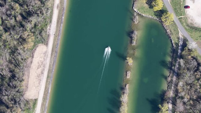 Aerial view of a solitary boat cutting through the tranquil, dark green waters of a canal bordered by lush green trees, Sausheim, Grand Est, France.