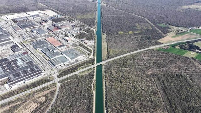 Aerial view of a canal dissecting an industrial complex on one side and fields and woodland on the other, a stark contrast of landscapes, Sausheim, France.