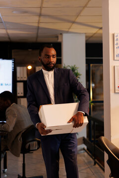 Stressed sad businessman getting fired from corporate job ready to leave office late at night. Upset executive manager packing personal belongings in cardboard box. Business concept