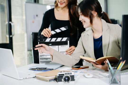 Creative team planning video production in modern office, using clapperboard, laptop and notebook. Business, marketing, content creation