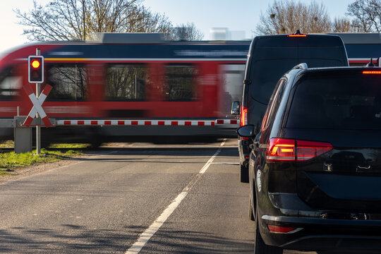 Cars waiting railway crossing passenger train passes motion blur clear daylight. Road barrier red signal transport infrastructure traffic stop safety rules railway transportation in rural Europe
