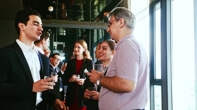 Professionals converse and network at a bright office event, holding drinks and smiling beside large windows