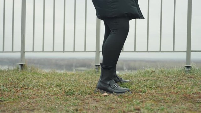 Solo dance outdoors. Caucasian legs dance on grass. Quiet solo practice with legs moving on damp ground. Lone dancer performs subtle routine on grassy surface beside metal barrier outdoors
