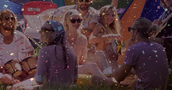 Friends sitting on grass by tents, guitarist starting music, celebrating, clapping, confetti rising