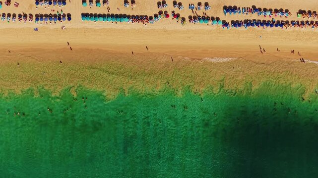 Aerial view of crowded beach shoreline with turquoise water and rows of umbrellas on sandy coast, Karon on Phuket island, Thailand.