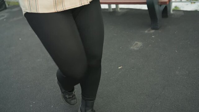 Street dance footwork on asphalt, closeup of woman legs in black leggings and worn boots, plaid coat hem visible, rhythmic stomps and precise steps, urban pavement texture and casual rehearsal energy