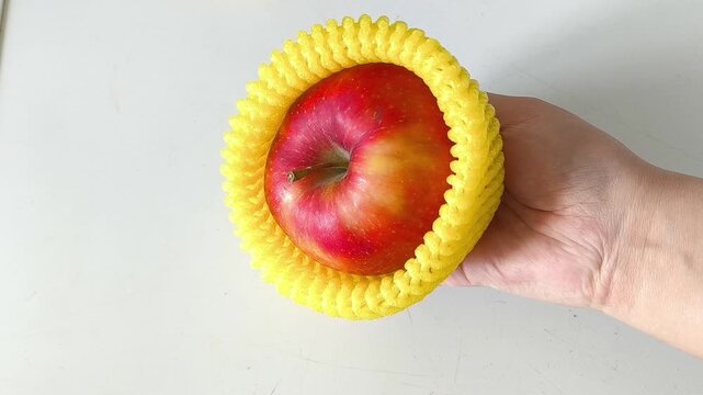 Close-up of an apple in a yellow foam net in your hand. Packaging for transportation, delivery of vegetables.