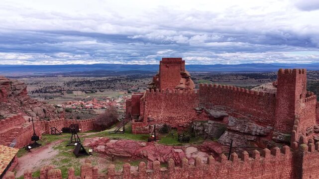 Castle of Peracense in Aragon, Spain &mdash; red stone medieval fortress with battlements, catapults, and sweeping valley views under cloudy skies