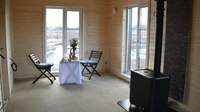 An empty room with wooden walls a window a small table two chairs fruit and a vase of flowers