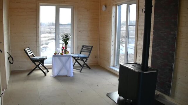An empty room with wooden walls a window a small table two chairs fruit and a vase of flowers