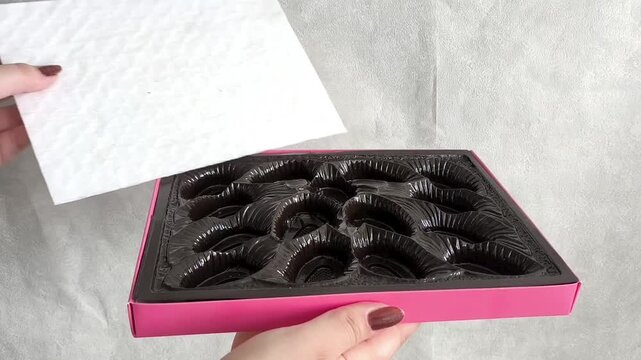 A woman's hand opens an empty box of chocolates. Confectionery Packaging