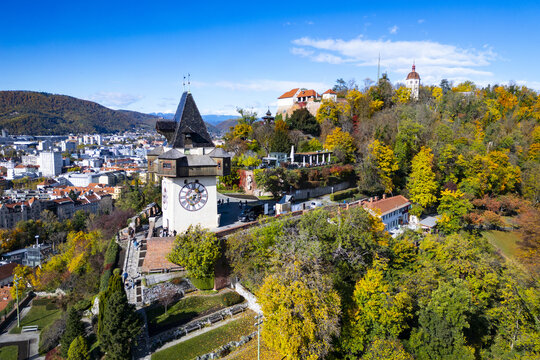Aerial view of the Grazer Uhrturm clock tower and Schlossberg hill, a blend of autumnal hues against the city skyline, Graz, Styria, Austria.