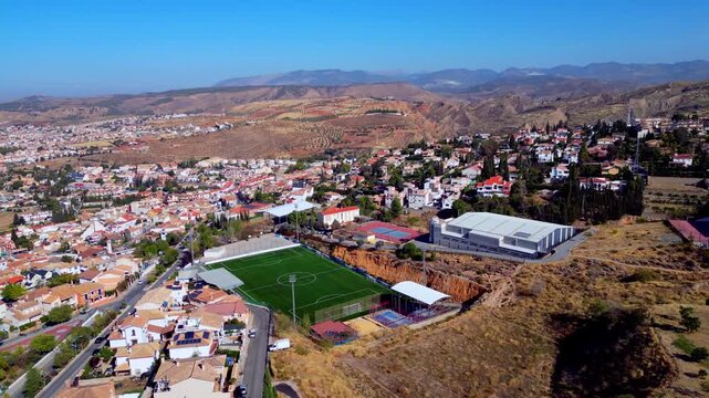 Soccer field in small town surrounded by mountains under blue sky, scenic landscape