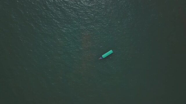 Aerial view of a single turquoise-colored boat floating on dark green ocean waters near Malvan, Maharashtra, India. The boat moves gently across the textured sea surface.
