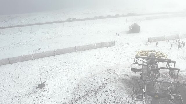Serra da Estrela ski resort under a blizzard, displaying a damaged chairlift station and infrastructure in heavy snow, with maintenance crew inspecting the site after the storm, overhead drone shot