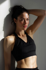 Fototapeta premium american fitness model in black athleisure outfit posing indoors, toned female athlete showcasing abs and strength in soft lighting, stylish sporty woman with defined muscles against minimalist wall