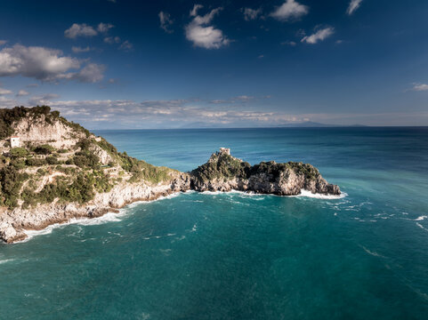 Aerial view of a rocky promontory with an ancient fortress juts into the turquoise sea under a vast sky, Amalfi, Campania, Italy.