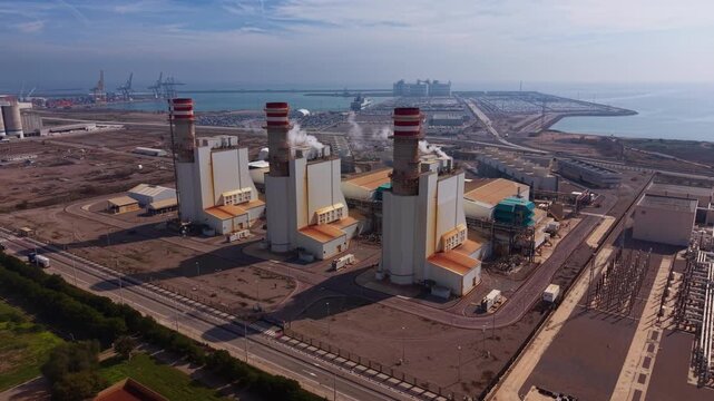 Combined cycle gas power plant with turbines, heat recovery steam generators and exhaust stacks near a coastal port and high-voltage transmission switchyard
