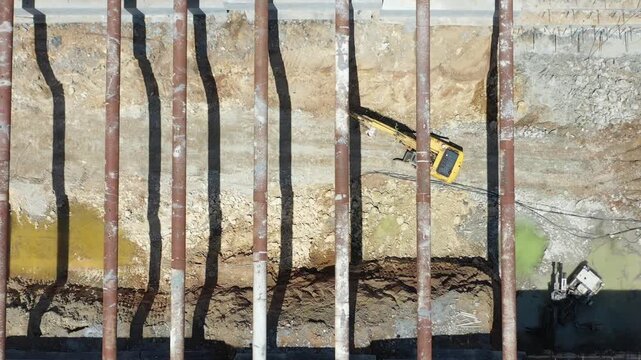 Drone shot of excavator and ground improvement machine working under steel strut pipes in deep foundation excavation. Shoring systems in engineering and heavy industry.