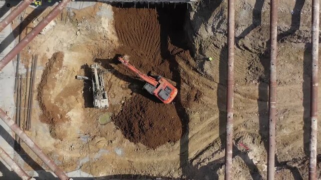 Drone shot of excavator and ground improvement machine working under steel strut pipes in deep foundation excavation. Shoring systems in engineering and heavy industry.