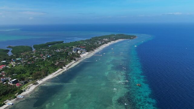 A drone pans right over Doljo Beach, showing reef flats and the curving coast in Panglao, Bohol