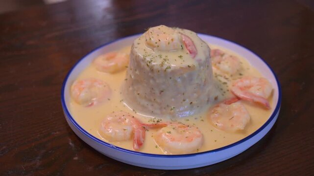 Cinematic high angle shot of a traditional Puerto Rican mofongo dish. Mashed green plantains served with succulent shrimp and sauce on a white ceramic plate