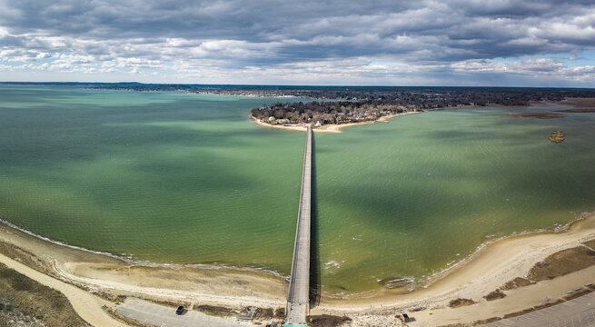 Aerial view of the Powder Point Bridge stretching across the turquoise waters to a wooded peninsula under a sky of textured clouds, Duxbury, Massachusetts, United States.