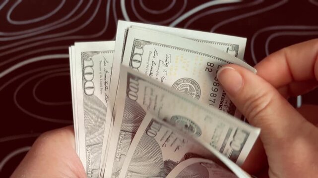 Woman hands flipping through stack of hundred dollar bills close up, counting cash money on dark background