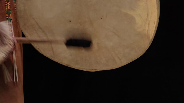 A close-up of a shaman rhythmically beating a traditional national drum with a stick against a black background. Mysticism and ethnic culture of Injuns and northern peoples of the world