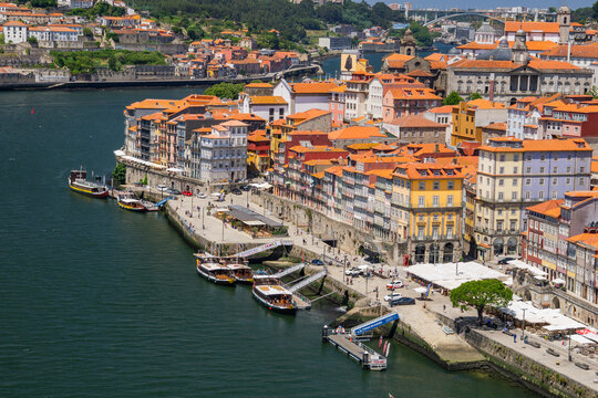 Aerial view of the vibrant Ribeira district's terracotta roofs cascading down to the Douro River, where boats bob gently in the deep blue water, Porto, Porto District, Portugal.