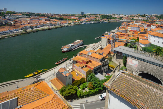 Aerial view of the Douro River snaking through Porto, lined with buildings boasting terracotta roofs, creating a vibrant contrast against the deep green waters, Porto, Porto District, Portugal.