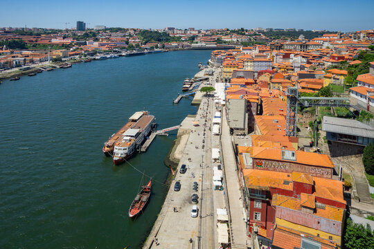 Aerial view of terracotta rooftops cascading down to the Douro River where boats bob gently, creating a tapestry of warm hues against the cool water, Porto, Porto District, Portugal.