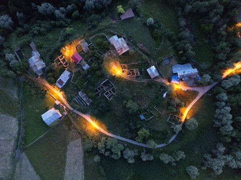Aerial view of warm lights illuminating the village homes nestled amidst the dark green forest, creating a cozy contrast, Posof, Ardahan, Turkey.