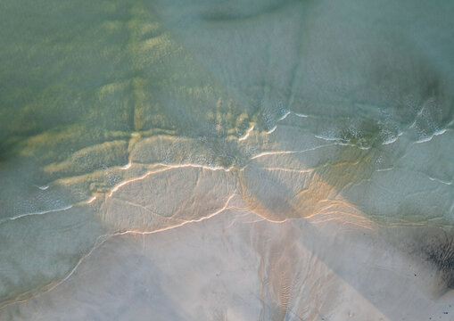 Aerial view of the mesmerizing dance of sunlight on gentle waves meeting the shore, creating a symphony of blues and sandy whites, Pantai Tanjung Aan, West Nusa Tenggara, Indonesia.