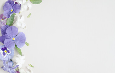 Fototapeta premium Vertical floral border of purple pansy, white jasmine and blue hyacinth on white background, soft petals texture, left-side composition, ample copy space
