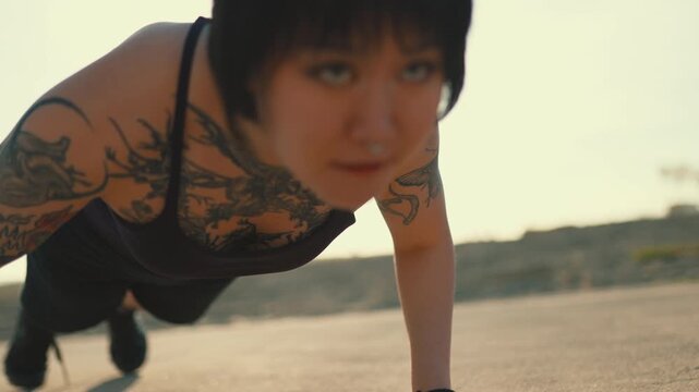 Tattooed athletic woman doing push-ups outdoors