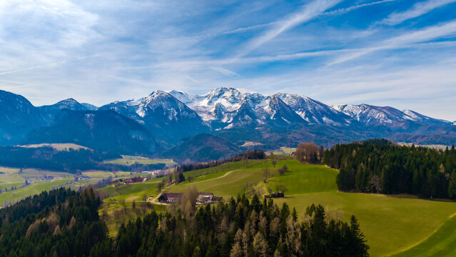 Aerial view of the valley's verdant patchwork quilt stretching towards the snow-capped mountains under a vast, azure sky, Windischgarsten, Upper Austria, Austria.