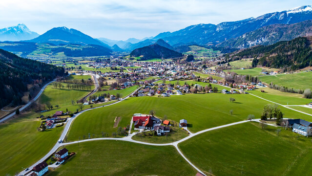 Aerial view of emerald green fields meeting quaint villages nestled beneath snow-capped mountains in the Windischgarsten valley, Windischgarsten, Upper Austria, Austria.