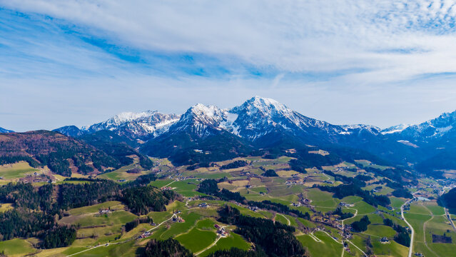 Aerial view of snow-capped mountains rise majestically over the lush green valley, creating a stunning contrast against the bright blue sky, Windischgarsten, Upper Austria, Austria.