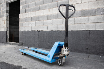 Blue hydraulic pallet truck positioned near an open doorway of a concrete block building under construction. © Roman