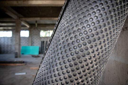 Close-up of black dimpled waterproof membrane roll at an indoor construction area for foundation and wall protection.