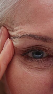 Close-up portrait: old woman face with grey hair, eyes. Concept of plastic surgery of the face, eyelid lift, blepharoplasty, cosmetology. Macro shot of senior female wrinkles near the eyes. Aging skin