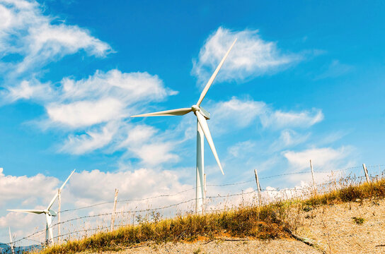 Wind turbine standing on a mountain ridge under a bright blue sky, symbolizing clean energy and natural harmony