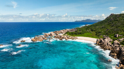 Fototapeta premium Granite coastline with clear turquoise waters, white sandy beach, and vibrant greenery. Anse Marron beach. La Digue, Seychelles.