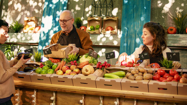 Vegetarian couple shopping at local farmers market on sunny day. Young man and woman standing at local produce counter looking at various locally grown organic fruits and vegetables.