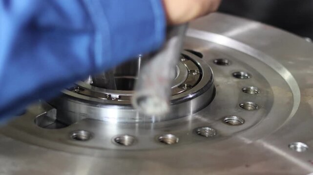 ​Mechanical technician installing a steel bearing into a heavy industrial metal component using a large hex bolt and hammer as manual tools inside a professional workshop.