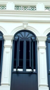 Close-up of elegant dark blue arched windows on a white historic building in Old Phuket Town, Thailand. Classic Sino-Portuguese architectural details, heritage shutters and colonial style facade.