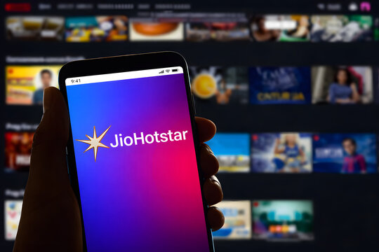 Hand Holding Smartphone Displaying JioHotstar App with Blurred OTT Content Interface Background, Digital Streaming Platform Concept