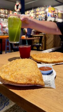 Large fried cheburek pastries with sauce and a red drink served on a wooden table inside a cozy cafe in Phuket, Thailand. Traditional Russian or Caucasian food street cafe scene. Travel cuisine.