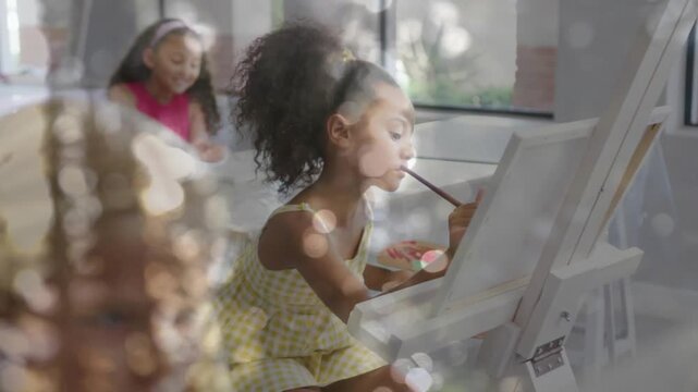 Camera pulling back, center girl in yellow dress dipping brush, painting canvas for art class